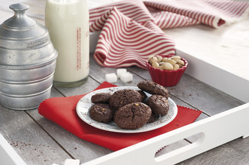 Rustic biscuits cocoa and pistachios on wooden tray with a bottle of milk, sugar bowl aluminum, fresh pistachios, sugar cubes and striped tablecloth