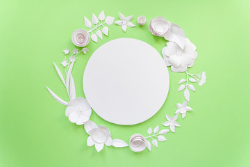 Round frame with white paper flowers on green background.