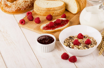 Healthy dietary breakfast with muesli, milk, fresh raspberries, jam and bun
