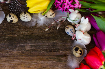 Spring easter frame with fresh flowers, eggs and rabbits close up with copy space on wooden desktop background