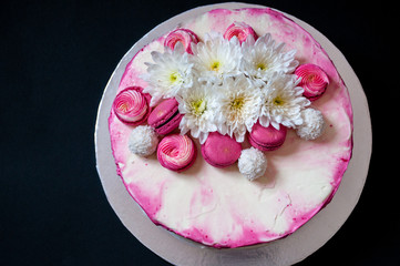 Obraz na płótnie Canvas Wedding cake with white spring flowers and macaroon on top. Delicious pink cake isolated on dark background.