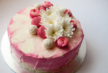 Wedding cake with white spring flowers and macaroon on top. Delicious pink cake isolated on white background.