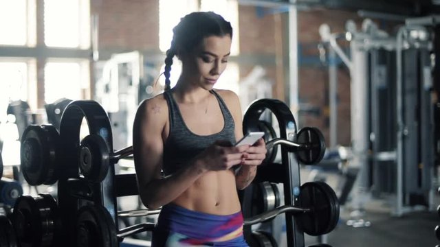 Fit young woman using cell phone at gym 