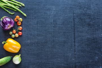 Fresh farm vegetables on a dark background. Bell pepper, tomatoes, eggplant, cucumber and asparagus. Space for text.