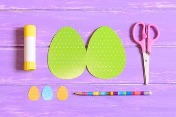 How to make Easter egg greeting card. Step. Guide. Colored cardboard pieces in shape of egg, scissors, glue stick, pencil on a wooden table. Children Easter paper crafts idea. Top view. Closeup