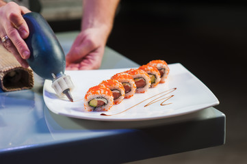 Cook serving california roll on white plate.