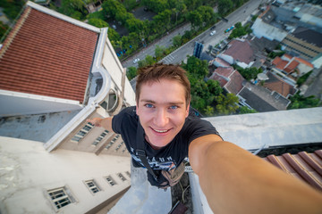 A young brave man, making a selfie on the edge of the roof of the skyscraper. Surabaya, Indonesia
