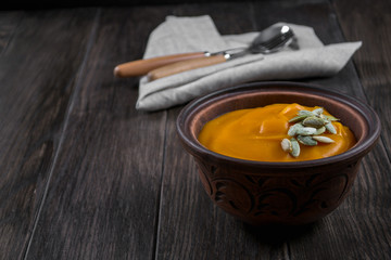 Pumpkin cream soup in a clay bowl on dark wooden  table
