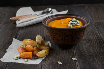 Pumpkin cream soup in a clay bowl with snack fried croutons bread,baked carrots.