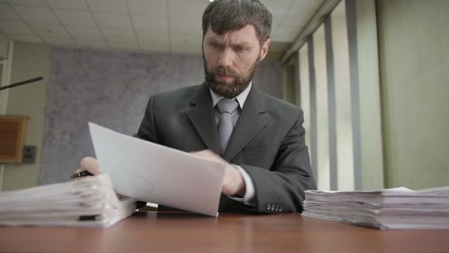 Busy office worker sadly shakes his head, signing and stamping incoming documents. businessman nobs and showe thumb to the top