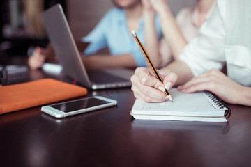 partial view of businesswoman writing notes with coworkers working near by