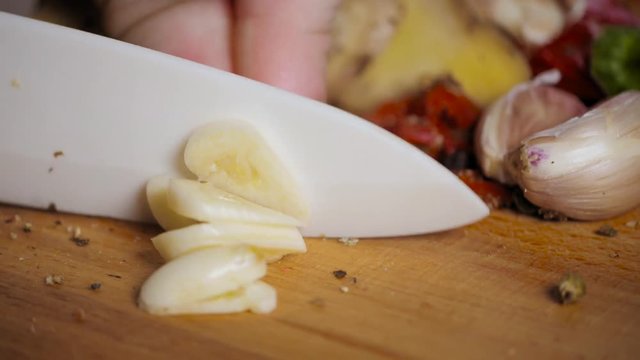 Close up cut garlic over wooden cutting board with knife, chile and pepper on background