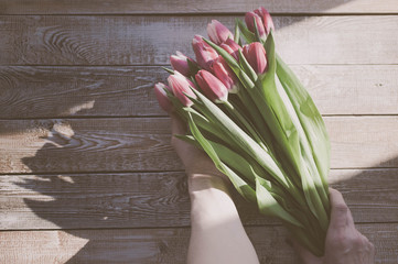 Graceful female hands hold a bouquet of red tulips over a wooden table. Soft retro toning