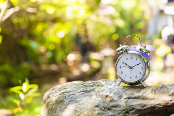 Retro clock on stone with tree and light bokeh background
