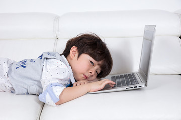 Tired Asian Chinese little boy playing laptop on the couch