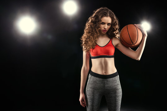 Beautiful young sporty woman in sportswear posing with basketball ball