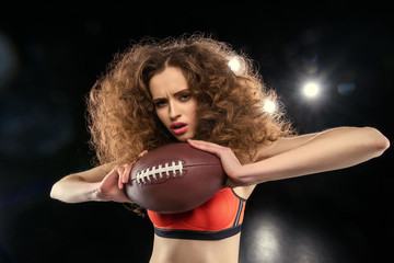 Attractive young sportswoman with culry hair holding rugby ball