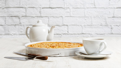 Homemade shortcake and cup of tea on white wooden table opposite a white brick wall. Italian crostata with orange and apple filling.