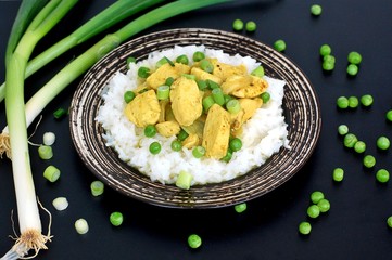 Chicken fillet with curry, green peas, spring onion and on dark plate on black background