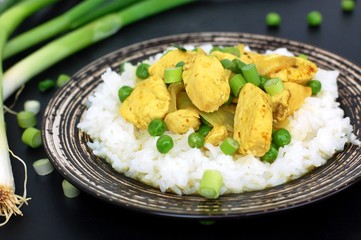 Chicken fillet with curry, green peas, spring onion and on dark plate on black background