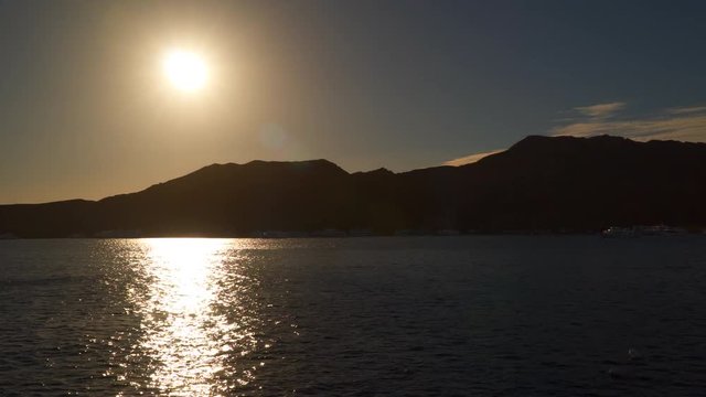 Reflection of the sun in the sea. You can see the silhouettes of mountains and boats