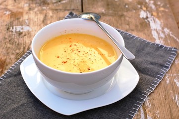 Soup from pumpkin and coconut milk in white bowl with spoon on grey cloth on rustic table