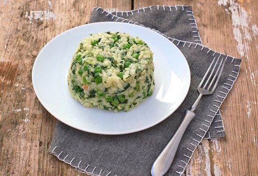 Creamy risotto with peas and spinach on white plate on grey cloth on rustic table