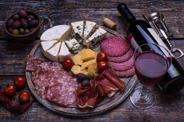 Red wine in a bottle, cork, bottle screw and a set of products - cheese, grapes, nuts, olives, tomatoes on a wooden board, background