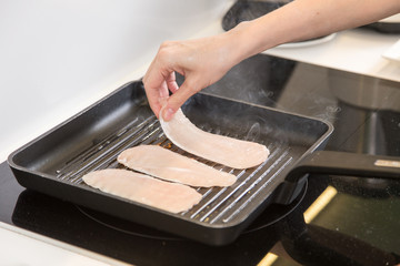 female frying chicken fillets in a frying pan