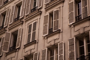 Obraz premium Low perspective of old dirty weathered vintage stucco apartment building exterior with rows of open and shut old fashion wood shutter window balcony in historic Europe
