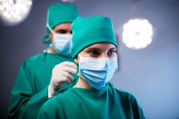 Surgeon helping a nurse in tying surgical mask in operation room