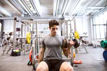 Hispanic man in gym sitting on bench, working out with weights