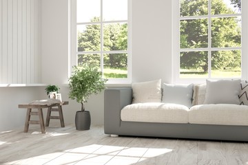 Fototapeta premium White room with sofa and green landscape in window. Scandinavian interior design. 3D illustration