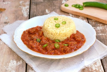 Perkelt from beef meat, peper and tomato with bulghur on white plate on wooden background
