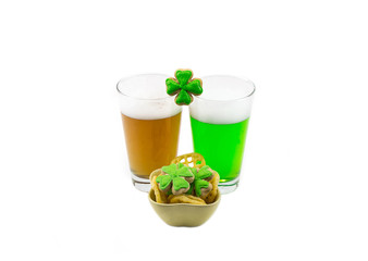 Two glasses of a foamy drink amber and green beer with a snack and clover on a white background St. Patrick's Day