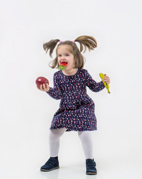 Ni&ntilde;a con coletas y  frutas en las manos saltando