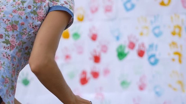 Young stylish pretty photographer check the result of photo shooting of cute child painting on the wall on color handprints background in slow motion 50fps
