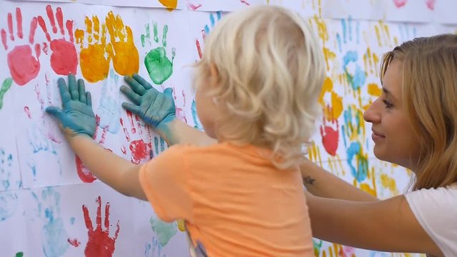 Close up of little cute child with mother making colorful handprints one side of hand and another on the white  wall in slow motion 50Fps."