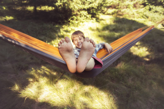 Smiling boy is swinging in a hammock. His feet are close up