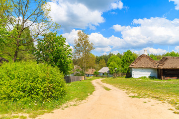 Rural road to Tokarnia village with straw roof houses on sunny spring day, Poland