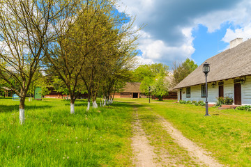 Rural road and old traditional house with straw roof in Tokarnia village on sunny spring day, Poland