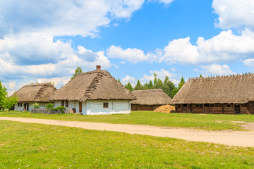 Fototapeta na wymiar Rural road and old traditional houses with straw roof in Tokarnia village on sunny spring day, Poland