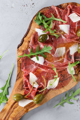 Beef carpaccio on olive wood serving board with capers, olive oil cheese and arugula, served over blue stone texture background. Top view with space for text.