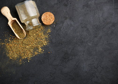 Zaatar - mix of Oriental spices on a dark stone background. Seasoning made from dried herbs, mixed with sesame seeds, sumac, salt and other spices. Top view.  Copy space. Selective focus