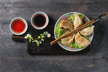 Gyozas potstickers on lettuce salad with sauces. Served in traditional china plate with chopsticks and spring onion on wood serving board over old metal background. Top view, space. Asian dinner