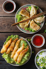 Fried tempura shrimps and gyozas potstickers on lettuce salad with sauces and rice. Served in traditional china plate with chopsticks over old wooden background. Top view. Asian dinner