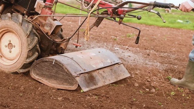 Farmer plowing the field with rototiller. Slow motion.