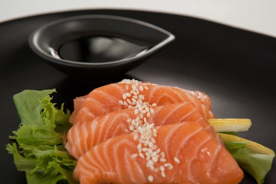 Four sashimi sushi served with soy sauce in black plate