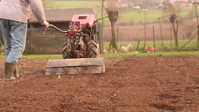 Farmer plowing the field with rototiller. 