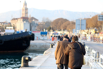 Fototapeta na wymiar Unrecognizable senior couple walking on a promenade in Split, Croatia during golden hour. Saint Domnius bell tower in the background. Selective focus. 